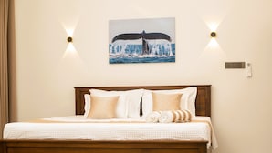 A neatly made bed with a wooden headboard, a wall-mounted picture of a whale tail, and two wall sconces. - Crescent Bay Weligama (Weligama)