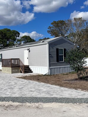 A single-story house with a covered porch and a small deck. - Pet Friendly Cozy 2-bedroom manufactured home with accessible feature's (North Fort Myers)