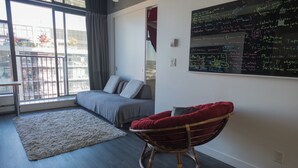 Un dormitorio moderno con un ventanal grande, una cama, una mecedora y una pared de pizarra con escritura.