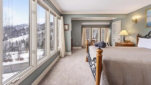 Ein Schlafzimmer mit großem Fenster, einem Bett, einem Nachttisch und Blick auf eine verschneite Landschaft.