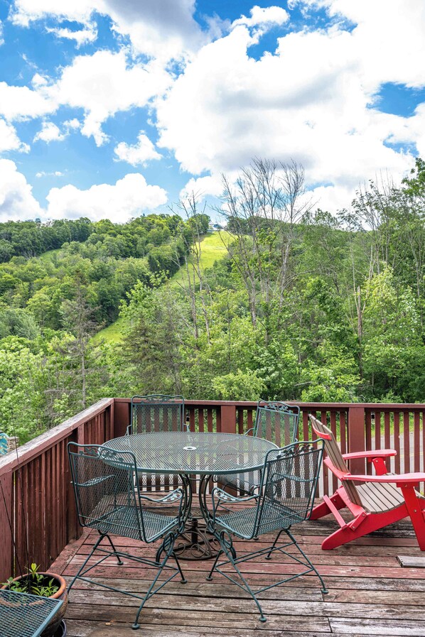 A deck with a table and chairs, overlooking a forested hillside.