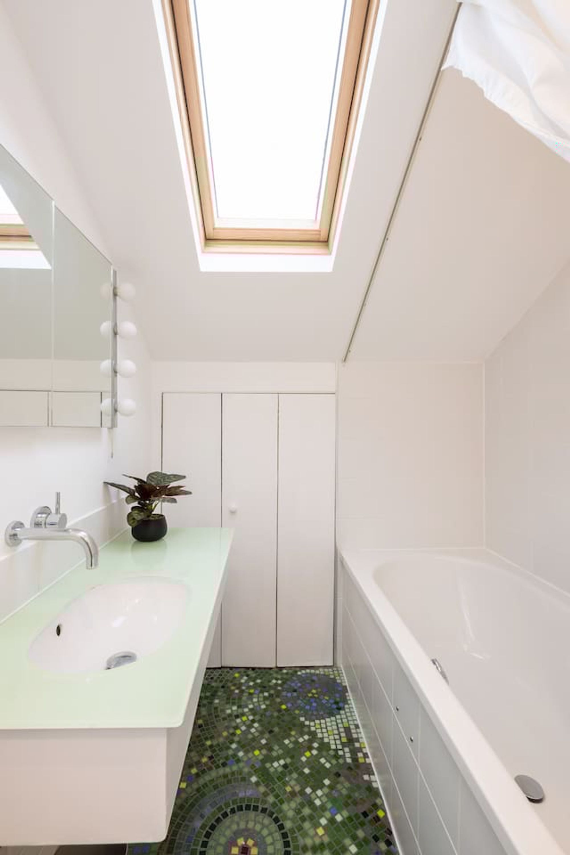 A modern bathroom with a skylight, a freestanding bathtub, and a mosaic-tiled floor.