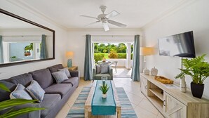 Ein modernes Wohnzimmer mit grauem Sofa, Couchtisch, Fernseher und Balkon mit Blick auf Grünflächen.