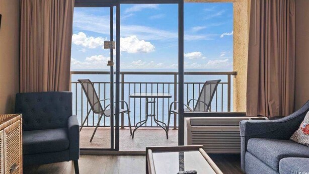 Ein Balkon mit Blick auf das Meer, eine Couch, ein Sessel und ein Tisch.