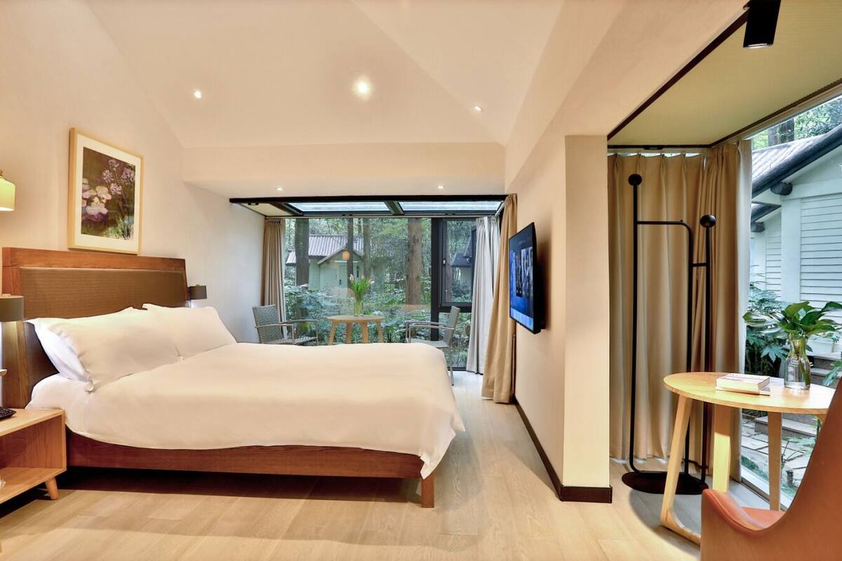 Habitación de hotel con una cama grande, un escritorio con lámpara, televisión y vistas al exterior.