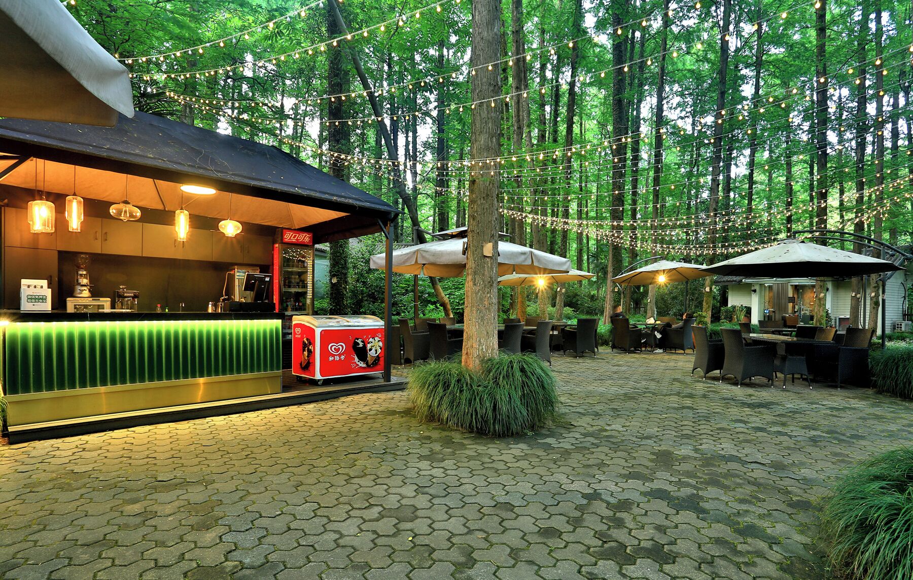 An outdoor café with hexagonal paving, string lights, and umbrellas.