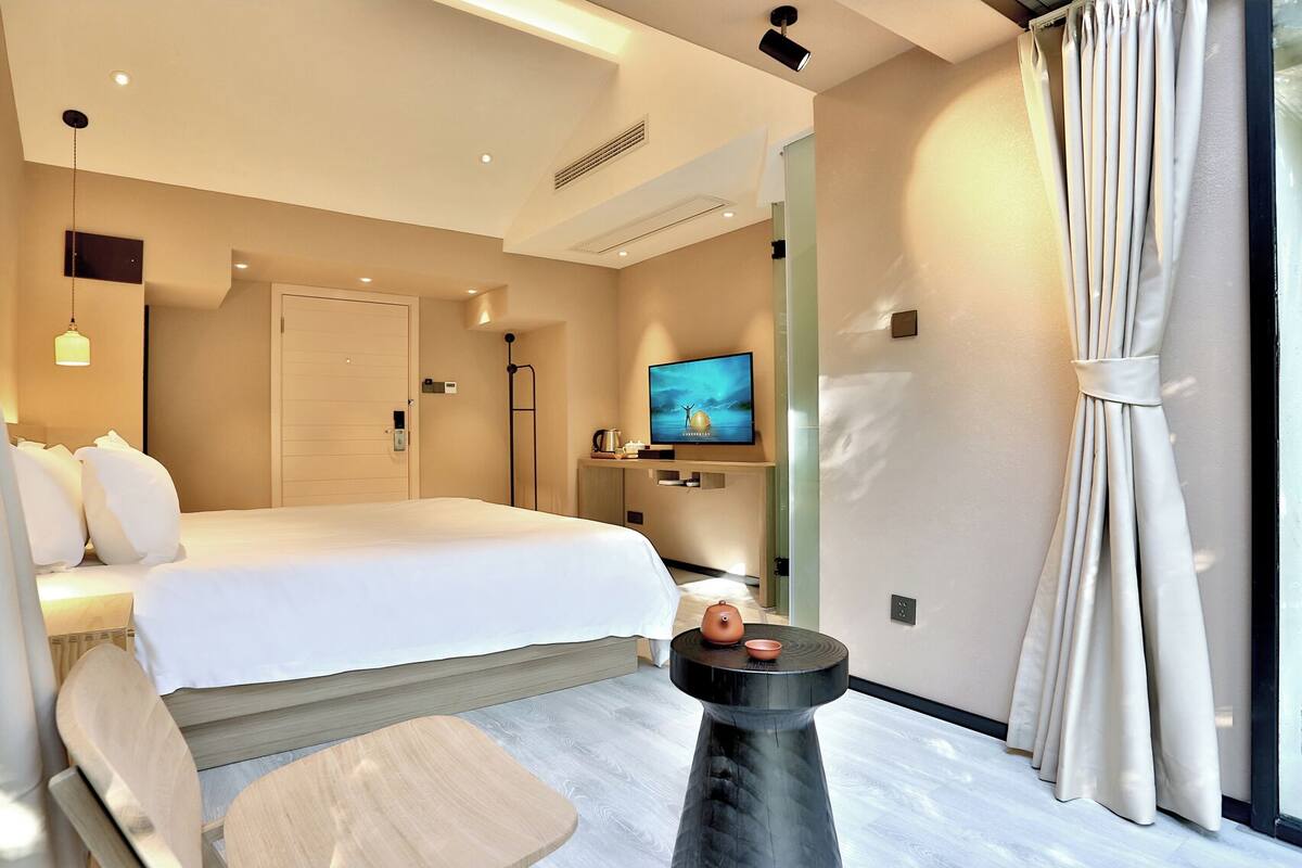 Habitación de hotel moderna con una cama grande, televisor, una mesita y ventana con cortinas.
