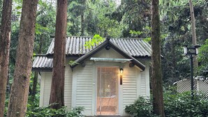 A small, single-story wooden cabin with a tiled roof, surrounded by tall trees and dense foliage. - Lotus Glade Hotel (Hangzhou)