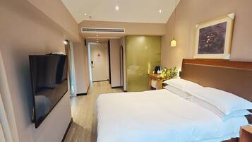 Una habitación de hotel con una cama grande, un televisor montado en la pared, una mesita de noche con una lámpara y un cuadro en la pared.
