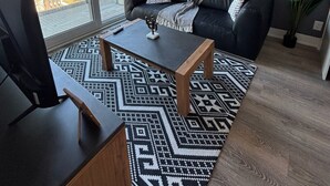 A modern living room with a black leather sofa, a wooden coffee table, and a patterned rug. There are three framed artworks on the wall and a large window offering a city view. - Modern 1BR Apt with Stunning Views and Pool Access (Toronto)