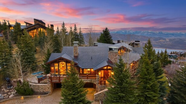 Un gran lodge de varios pisos con fachada de piedra, varias chimeneas y una terraza con vistas a un paisaje montañoso.