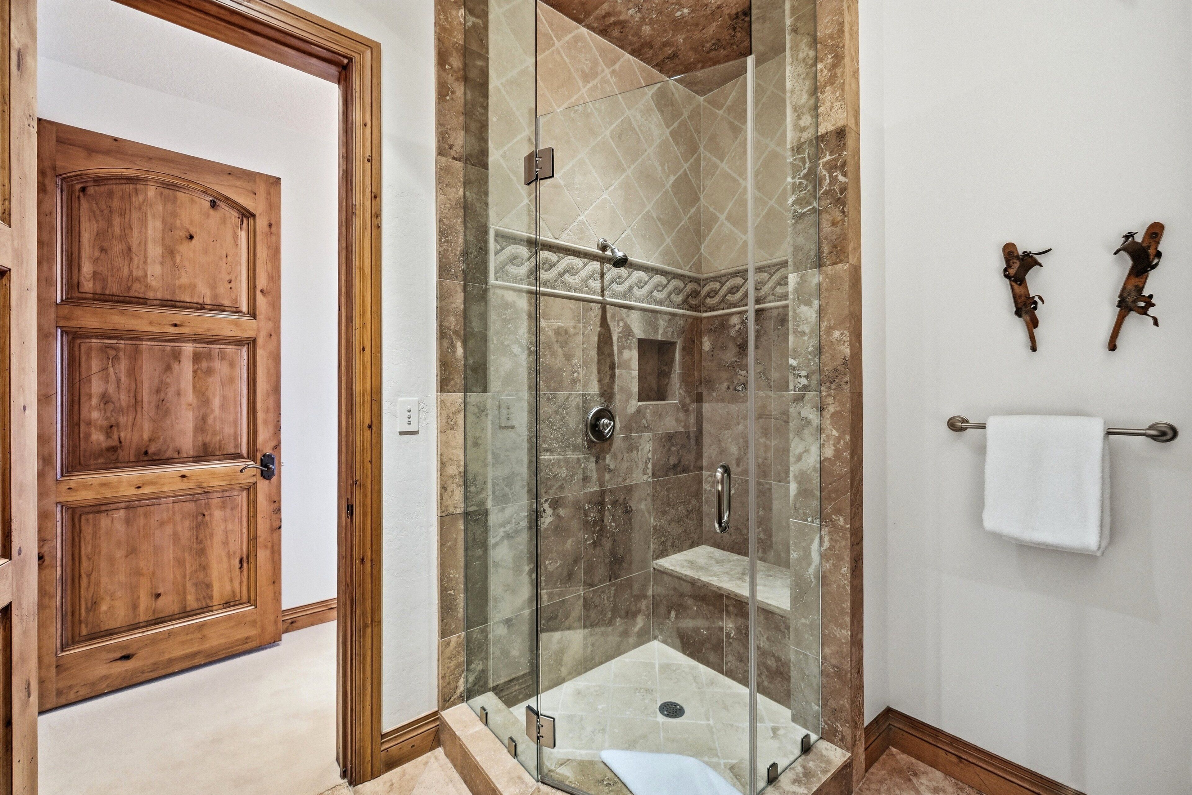 Una puerta de madera, una ducha con paredes de vidrio y azulejos, y un perchero con una toalla blanca.