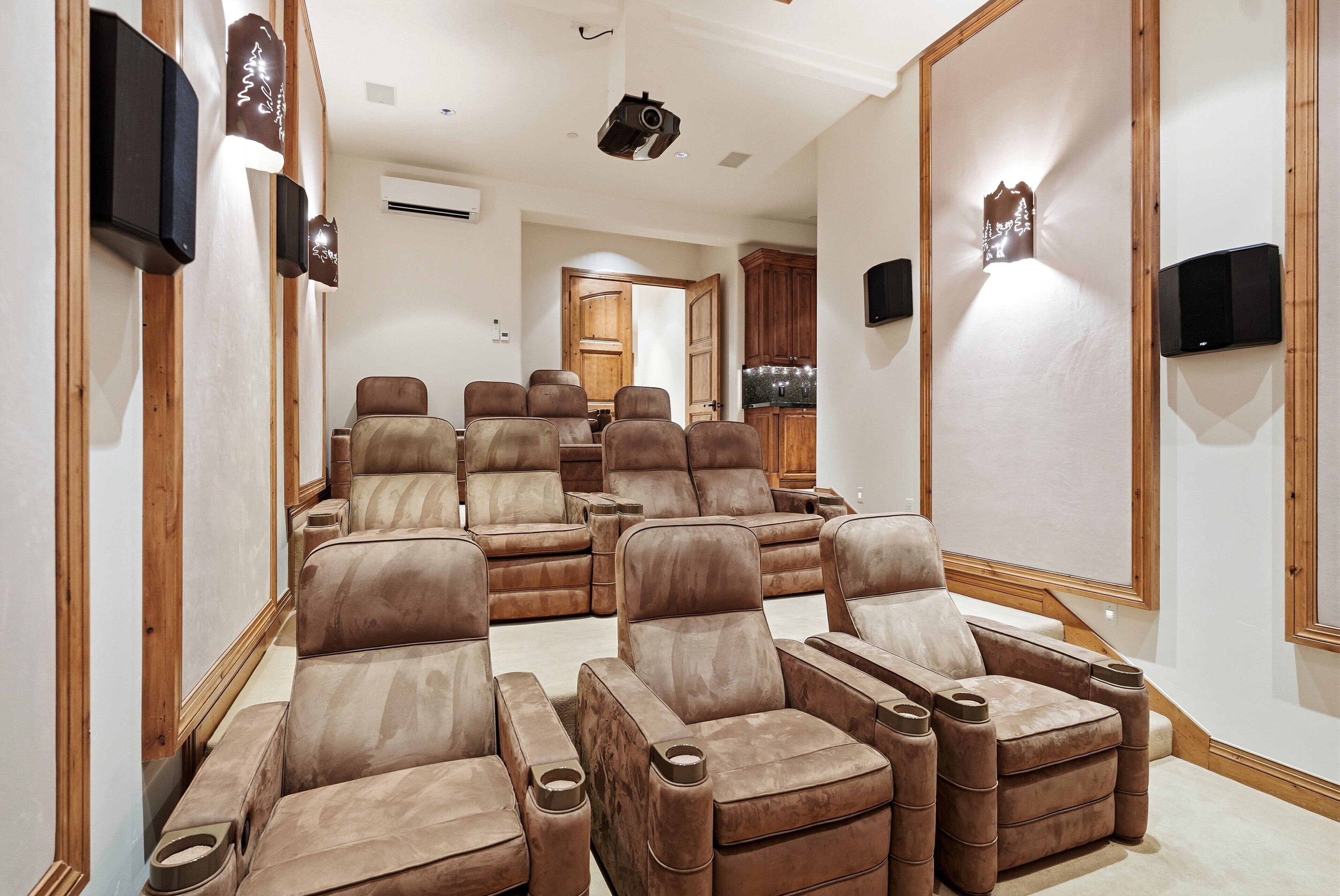 Una sala de cine en casa con varios sillones de cuero reclinables, un panel de madera y una cocina al fondo.