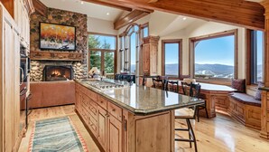 Una cocina amplia con una isla grande, chimenea de piedra y ventanas panorámicas con vistas a la montaña.