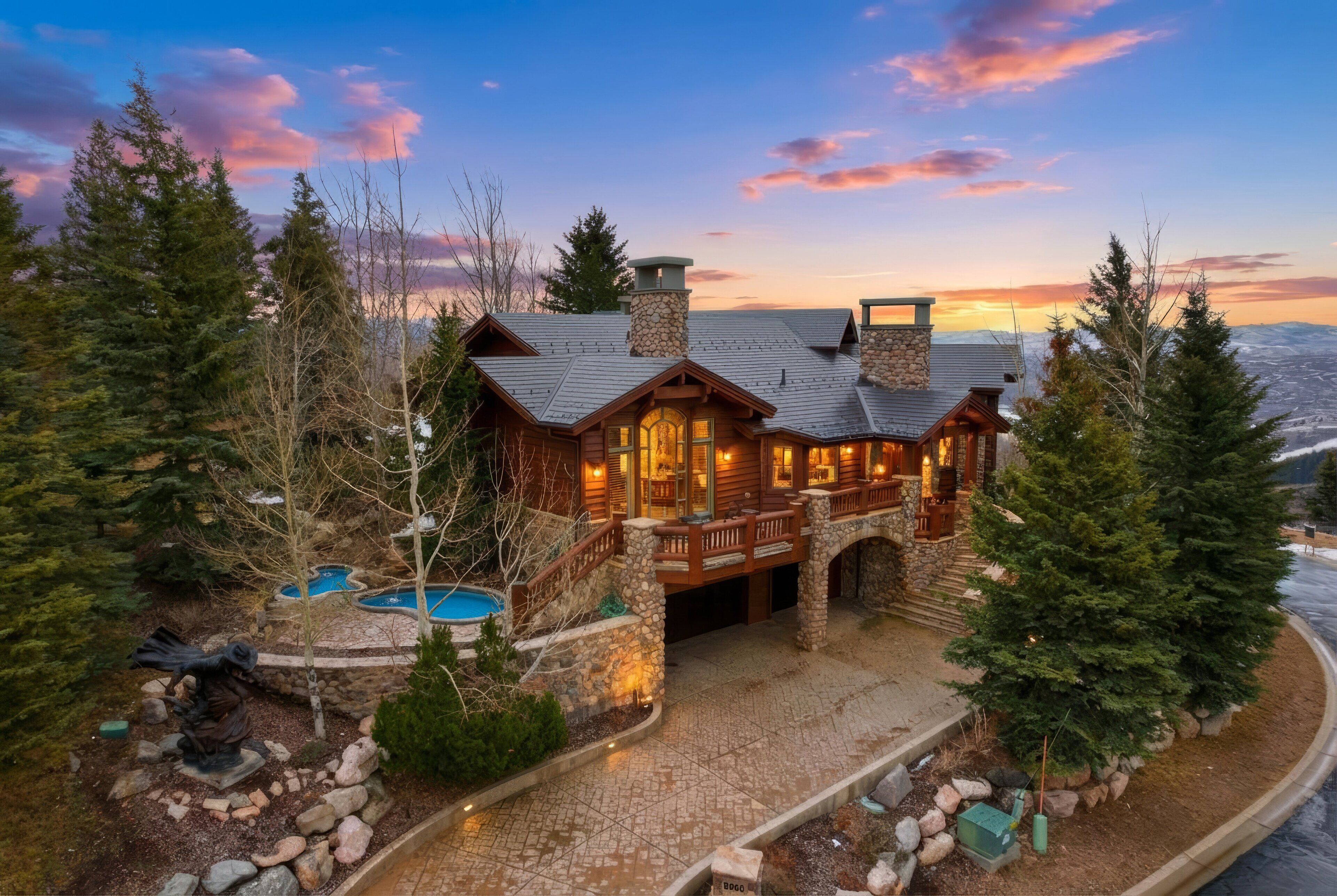 A large, multi-story log cabin with a stone chimney, a stone porch, and a swimming pool.
