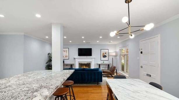 A modern kitchen with a marble island, bar stools, a fireplace, and a dining area with a table and chairs. - Marbella Lane - Immaculate & Cozy 3BR Home (San Jose)