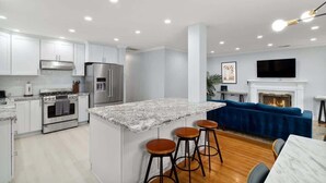 A modern kitchen with white cabinets, a stainless steel refrigerator, and a marble island with bar stools. - Marbella Lane - Immaculate & Cozy 3BR Home (San Jose)