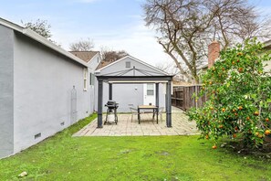 Ein Garten mit überdachter Terrasse, Grill und Tisch.