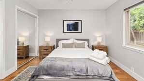 A bedroom with a large bed, bedside tables with lamps, a framed picture on the wall, and a window with a view of greenery. - Marbella Lane - Immaculate & Cozy 3BR Home (San Jose)
