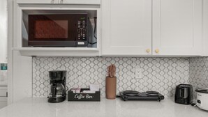 Een keuken met witte kastjes, een magnetron, een koffiezetapparaat, een broodrooster en een bord met daarop 'Coffee Bar'.