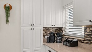 A kitchen with white cabinets, a coffee station, and a hanging plant. - Beautiful East Orlando Home Near Everything (Orlando)