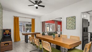 A modern dining area with a wooden table and green upholstered chairs, a ceiling fan, and a view of a red room through an open door. - Beautiful East Orlando Home Near Everything (Orlando)