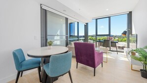 A modern living room with a round table, two blue chairs, a purple armchair, and a view of the outdoors through large windows. - Stylish 1BDR Sunlit Apartment w Rooftop Pool and Gym (Canberra)