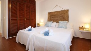 Een hotelkamer met twee bedden, een grote houten garderobe, een geweven wandtapijt en bedlampjes.