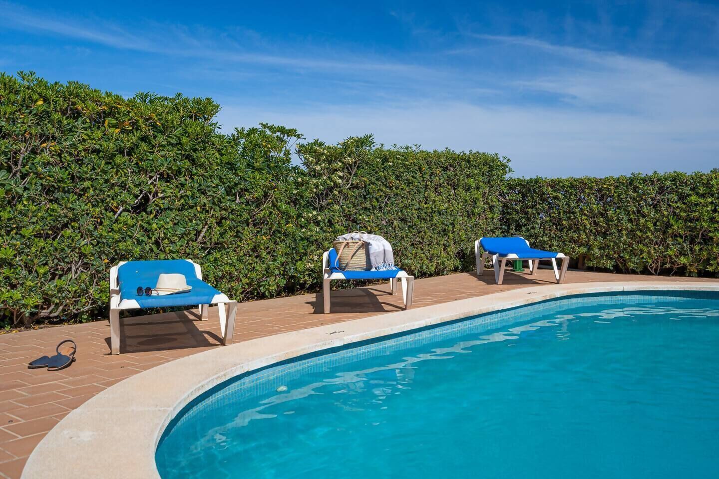 Zona de piscina con tres sillas de descanso y un seto al fondo.