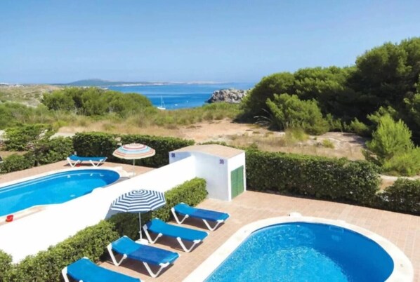 A swimming pool with lounge chairs and umbrellas, surrounded by greenery and a view of the sea.