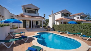 A swimming pool with lounge chairs and umbrellas, surrounded by a white building with a tiled roof. - Villa Las Marinas 3, pool and 5 minutes to the sea (S'Arenal D'En Castell (Menorca) (Urbanitzacio))