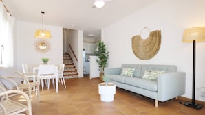A living room with a sofa, dining table, chairs, and a staircase leading to a kitchen. - Villa Las Marinas 3, pool and 5 minutes to the sea (S'Arenal D'En Castell (Menorca) (Urbanitzacio))