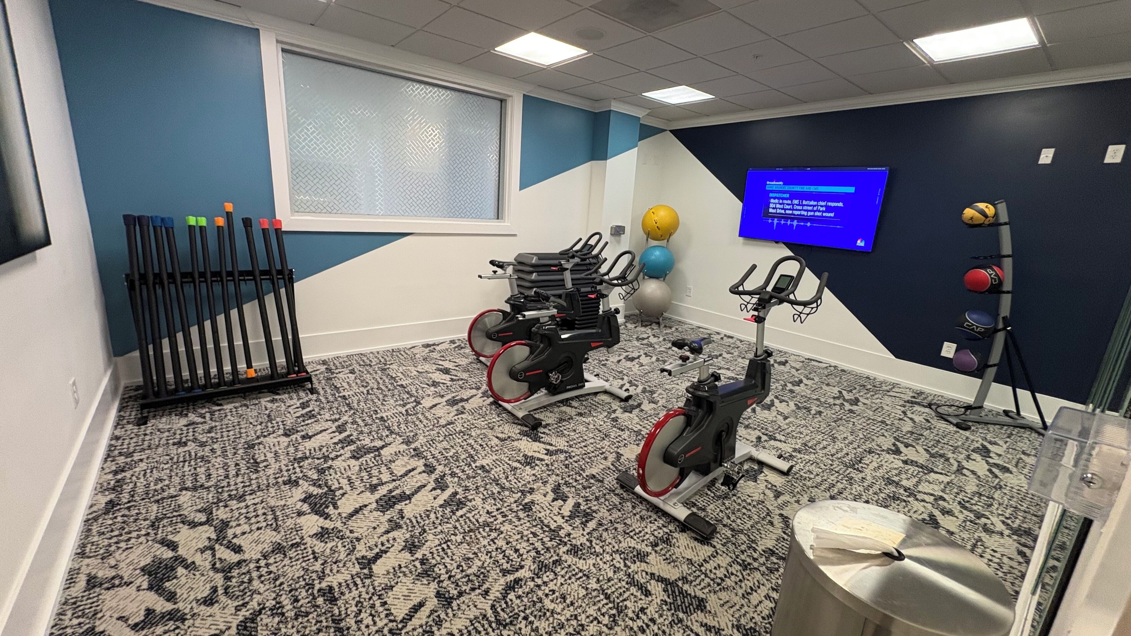 A room with a stationary bike, a treadmill, and a wall-mounted TV displaying a workout program.