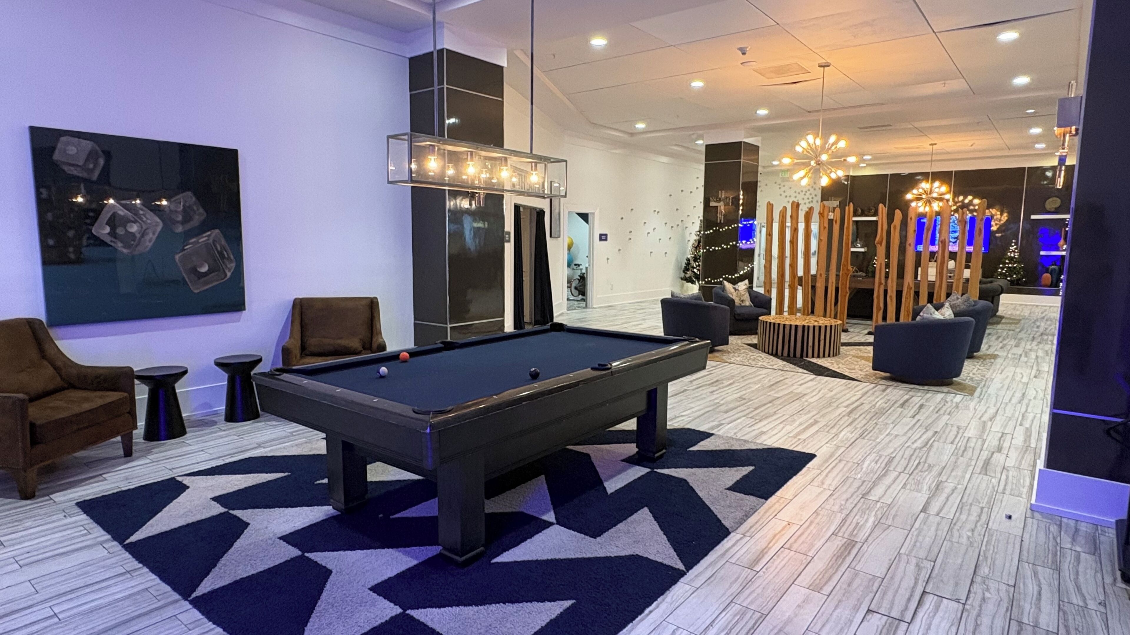 Una mesa de billar en un salón moderno con un suelo de diseño geométrico, asientos cómodos y un árbol de Navidad al fondo.