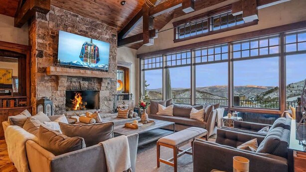 A spacious living area with a stone fireplace, comfortable seating, and large windows offering a view of the landscape. - Abode at Mountains Edge, ski-in/ski-out, hot tub, pool table (Park City)