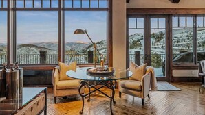 A room with a glass table, two chairs, a lamp, and a view of snow-covered hills. - Abode at Mountains Edge, ski-in/ski-out, hot tub, pool table (Park City)
