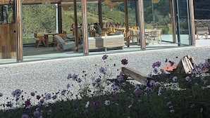 A modern outdoor seating area with glass walls, wooden furniture, and a view of snow-capped mountains. - Siguniang Mountain Wind-Waiting Homestay (Ngawa Autonomous Prefecture)