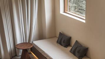 Habitación de esquina con cama, una mesita de madera y ventana con vista a un muro de piedra.