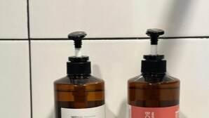 Dos botellas de champú sobre un estante negro frente a una pared de azulejos.