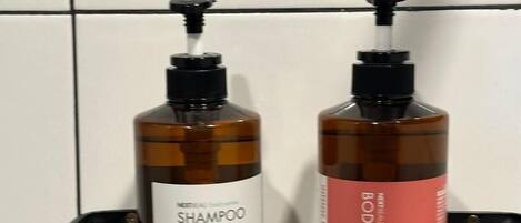 Two bottles of shampoo on a black shelf against a tiled wall.