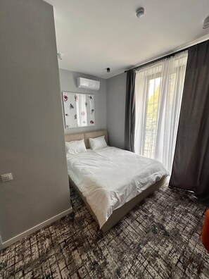 A hotel room with a bed, a wall-mounted air conditioner, and a window with curtains.