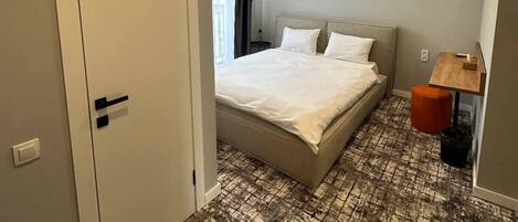 A bedroom with a bed, a small table, a chair, and a wall-mounted artwork.