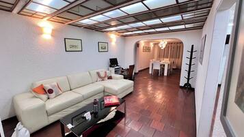 A living room with a sectional sofa, a glass coffee table, and a dining area with a table and chairs.