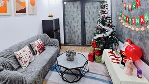 Ein Wohnzimmer mit grauem Sofa, einem Couchtisch, einem Weihnachtsbaum und einer Wand mit einem 'Merry Christmas'-Banner.