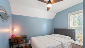 Ein Schlafzimmer mit Bett, Schreibtisch, Stuhl, Deckenventilator und Fenster.