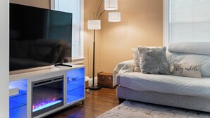 Una sala de estar moderna con un televisor de pantalla plana sobre un mueble bajo, una lámpara de pie, un sofá con cojines estampados y una alfombra decorativa.