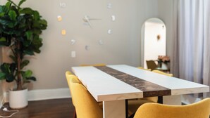 Un comedor con una mesa, sillas, una planta en maceta y un reloj de pared.