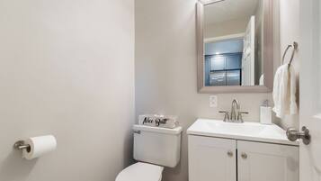 A bathroom with a toilet, sink, mirror, and a box labeled 'Nice Butt' on the toilet tank.