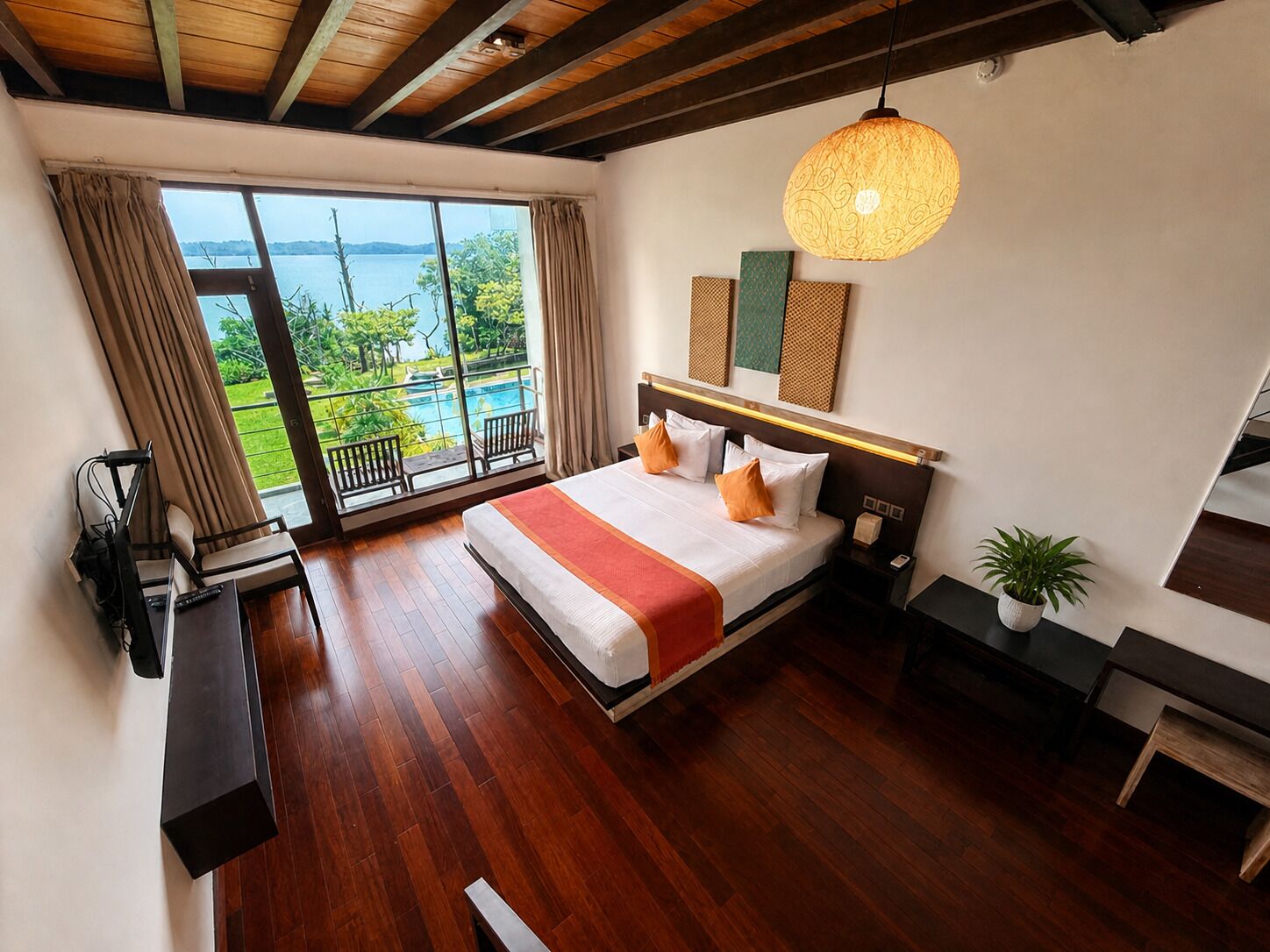 A bedroom with a large bed, a TV, a desk, and a balcony with a view of the water.