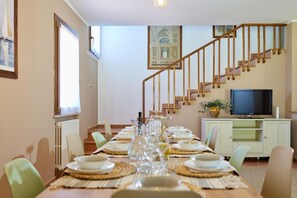 A dining area with a long table set for a meal, a staircase, a television, and a framed picture on the wall.